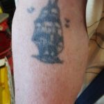 Överarmestatuering med segelfartyg och fågelsiluetter.