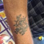 Underarmstatuering med gulröd ros med själk och blad.