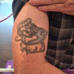 Överarmstatuering med barbröstad pinuppa, byst, iklädd matrosmössa och -halsduk.