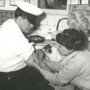 Svartvitt foto av en stilig, mörkhårig kvinna som tatuerar en sjöman i skärmmössa på högra överarmen.