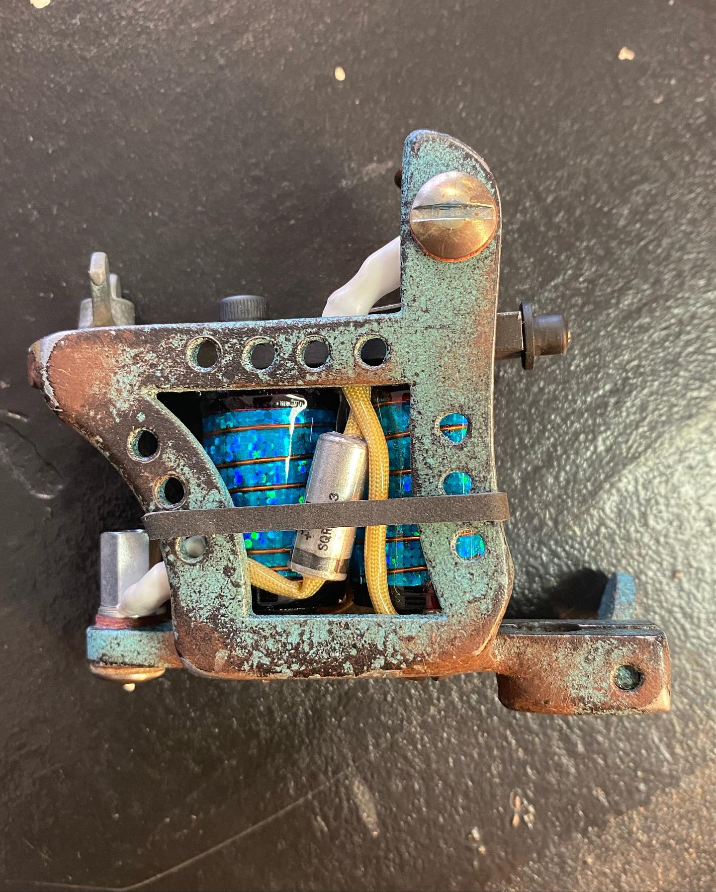 Klassisk coil-tatueringsmaskin med spolar, lackad i rost och turkos, tillverkad av Niklas Hanell.