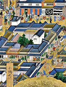 Målad tavla av 1600-talets Edo. Uppifrån ses en gatuvy av ett stadskvarter med ljusa höga trähus med blåsvarta tak. Små figurer av människor i färggranna kläder rör sig mellan byggnaderna.