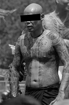 Svartvitt foto av yakuza-medlem – en man med täckt ansikte i bar överkropp täckt av traditionella japanska tatueringar.