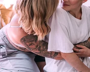 Närbild på två tatuerade personer som kramar varandra.