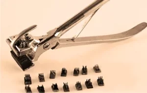 Klamptång med rektangulära huvuden mellan vilka materialet som ska märkas sticks in. Vid tången ligger flera små stansar med rektangulär fot. I varje sådan sitter en uppsättning grova nålar och bildar en siffra. När dessa sätts in i tången kan tången stansa in en serie siffror i materialet.