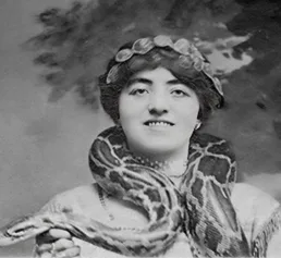 Svartvit porträttbild av Stuertz hustru, Dagmar Franciska Hansen, vid Barnum & Bailey Circus, 1913. En mörkhårig kvinna, med håret uppsatt enligt 1910-talets mode, med mörka ögon, bär en stor boaorm runt halsen. Hon ler mot kameran.